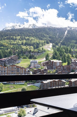 A mountainous landscape with a town featuring multi-story buildings with balconies, surrounded by dense forest and a clear sky. - Panoramic view, 2 bedrooms, covered parking (Nendaz)