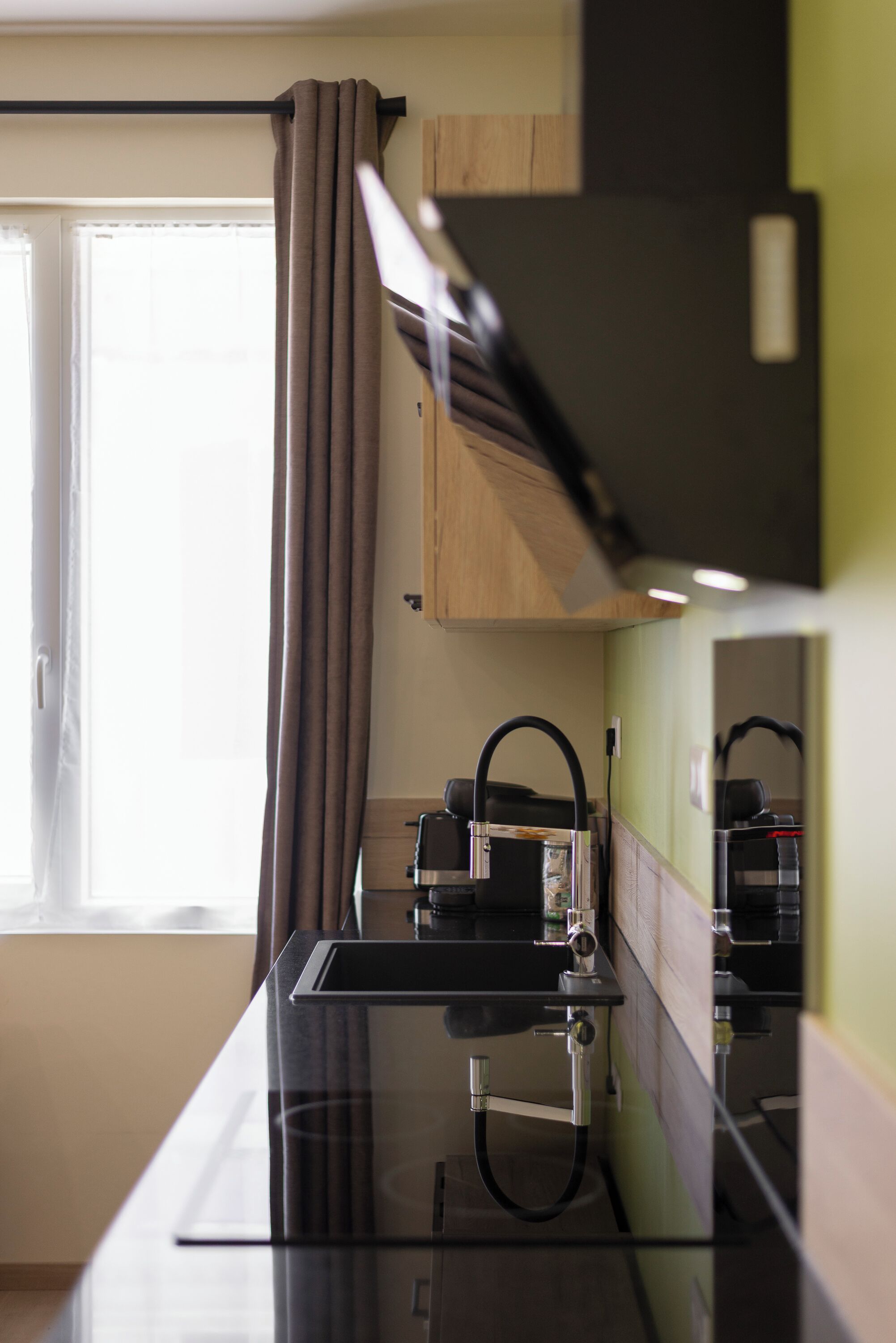 A modern kitchen with a glass countertop, a built-in oven, and a window with curtains.