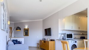 A modern living room with a sofa, a dining table, a TV, and a kitchen with appliances. - #357 Sea View Getaway in Portimão | Pool & Spacious (Portimão)