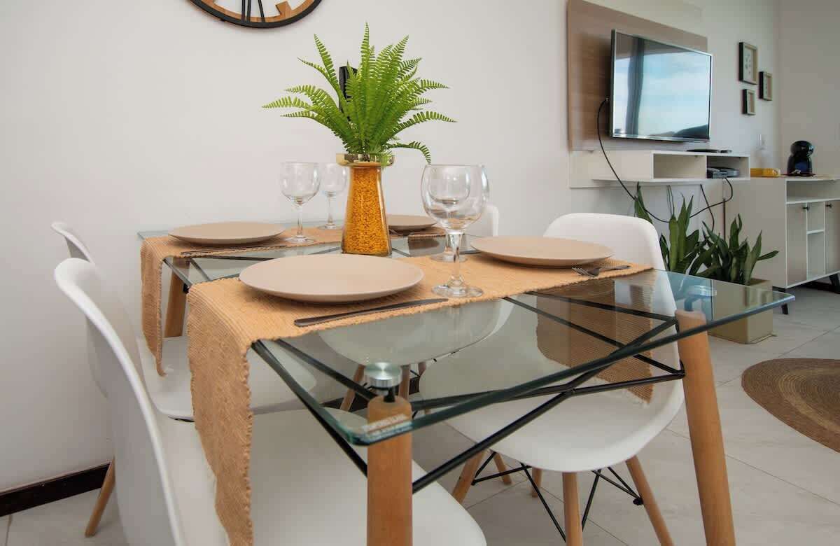 A dining area with a glass table, white chairs, and a plant centerpiece.