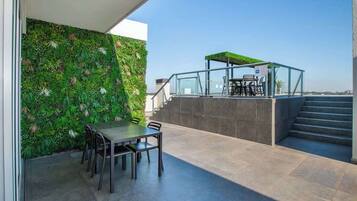 Eine Dachterrasse mit Esstisch und Stühlen, einer Glasumlaufung und einer grünen Wand.
