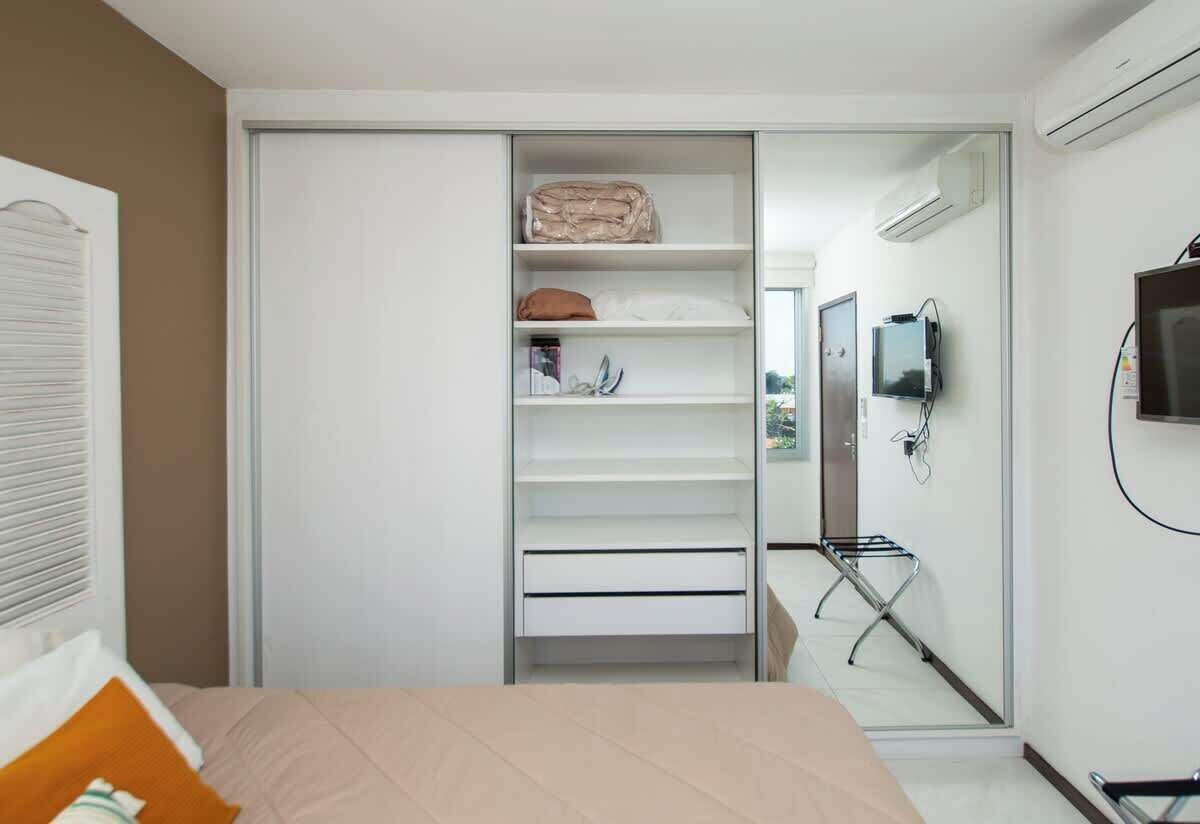 Un dormitorio con cama, armario con estantes, televisor y ventana.