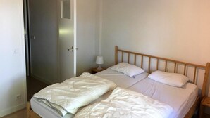 Quarto com uma cama de solteiro, mesa de cabeceira com abajur e porta que dá para outro cômodo.