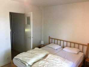Een slaapkamer met een enkel bed, een nachtkastje met een lamp, en een deur naar een andere kamer.