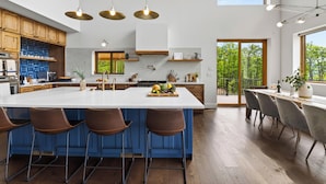 Une cuisine moderne dotée d’un grand îlot central, de tabourets de bar et offrant une vue sur la verdure environnante.