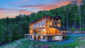 Une cabane en bois à plusieurs étages, dotée d’un balcon et entourée de forêt.