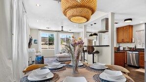 A dining area with a round table set for four, surrounded by patterned placemats, a vase with flowers, and a modern pendant light. - Pool + Firepit + BBQ | Near Park + DT Yucca Valley |  The Light of the Desert (Yucca Valley)