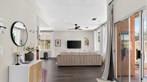 A modern living room with a sofa, TV, ceiling fan, and a large sliding glass door leading to an outdoor area. - Pool + Firepit + BBQ | Near Park + DT Yucca Valley |  The Light of the Desert (Yucca Valley)