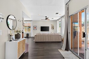 Ein modernes Wohnzimmer mit einer Couch, einem Fernseher, einem Deckenventilator und einer großen Schiebeglastür, die zu einem Außenbereich führt.