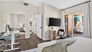 A modern hotel room with a bed, desk, chair, TV, and a view of the outdoor area. - Pool + Firepit + BBQ | Near Park + DT Yucca Valley |  The Light of the Desert (Yucca Valley)