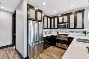 A modern kitchen with stainless steel appliances, dark wooden cabinets, and a white countertop. - Private Hot Tub + BBQ + Communal Pool | Walk to Lifts | Blackstone Chalet (Park City)
