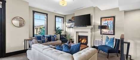 Una sala de estar con un sofá modular, un televisor de pantalla plana, una chimenea y un ventanal grande.