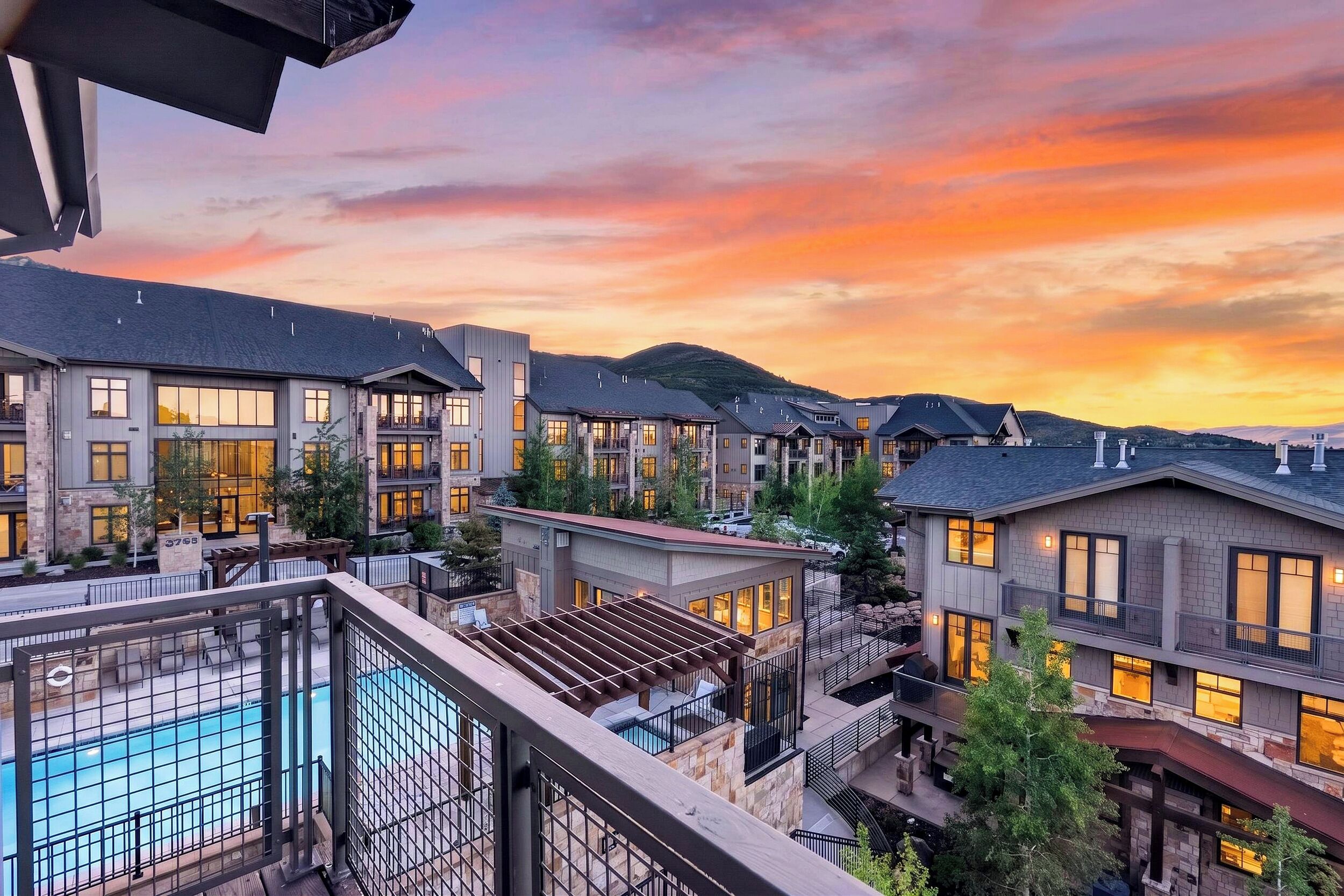A multi-story hotel with balconies, a pool, and a mountainous backdrop.