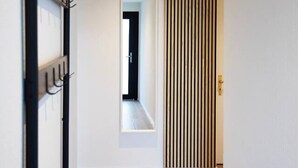 A hallway with wooden flooring, a coat rack, a vertical striped panel, and a door leading to another room. - Stunning, bright apartment with a private garden (Farvagny-le-Grand)