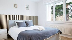 A modern bedroom with a bed, bedside table, and a window with a view. - Stunning, bright apartment with a private garden (Farvagny-le-Grand)