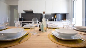 A modern kitchen with white cabinets, a wooden dining table set with white plates, glasses, and a bottle. - Stunning, bright apartment with a private garden (Farvagny-le-Grand)