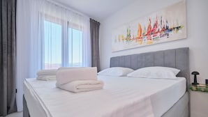 A neatly made bed with white linens and towels, a grey headboard, and a wall-mounted painting of sailboats. - Apartment Maestral (Ražanj)