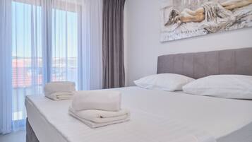 A hotel room with a bed, pillows, a painting on the wall, and a window with curtains.