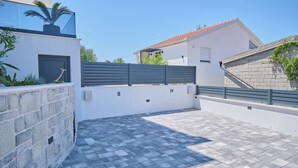 A modern outdoor patio area with a paved floor, a low stone wall, and a metal fence. - Apartment Maestral (Ražanj)