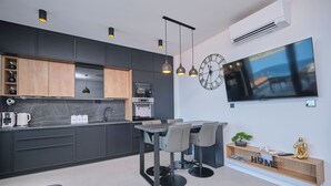 A modern kitchen with built-in appliances, a dining area with a table and chairs, and a large flat-screen TV mounted on the wall. - Apartment Maestral (Ražanj)