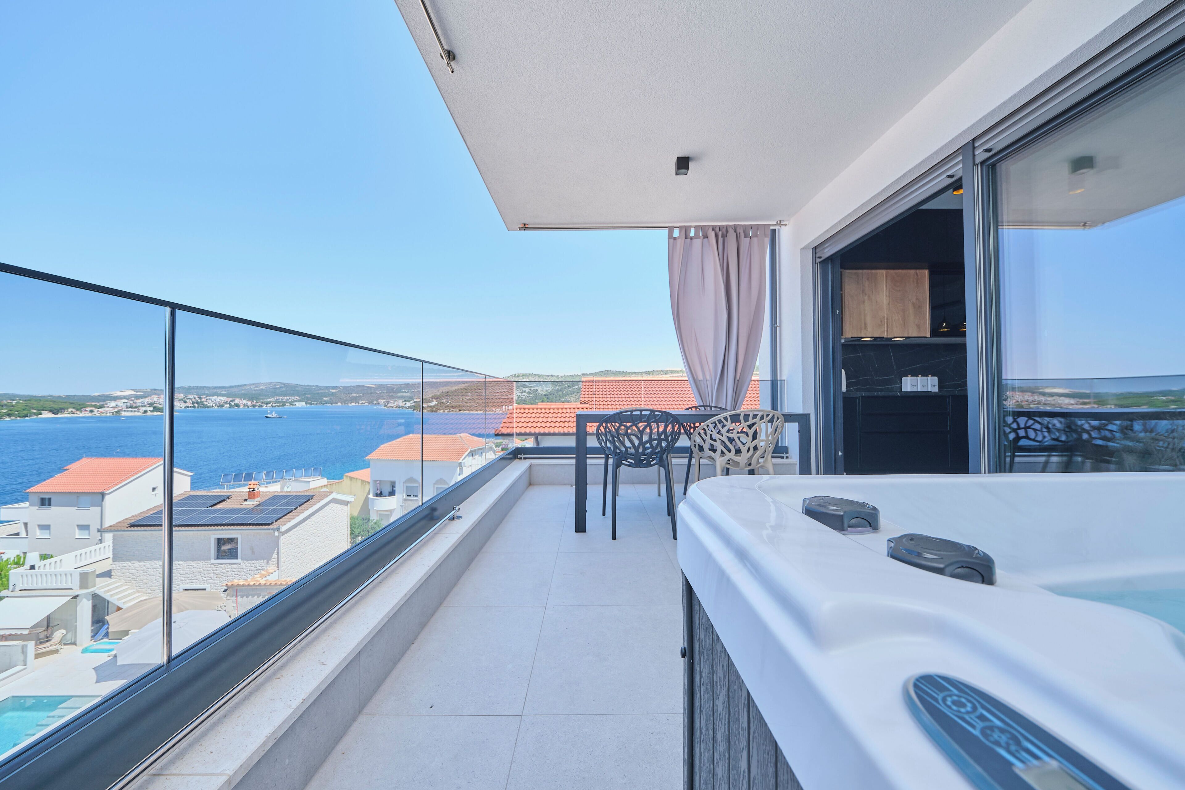A balcony with a view of the sea, a table with chairs, and a hot tub.