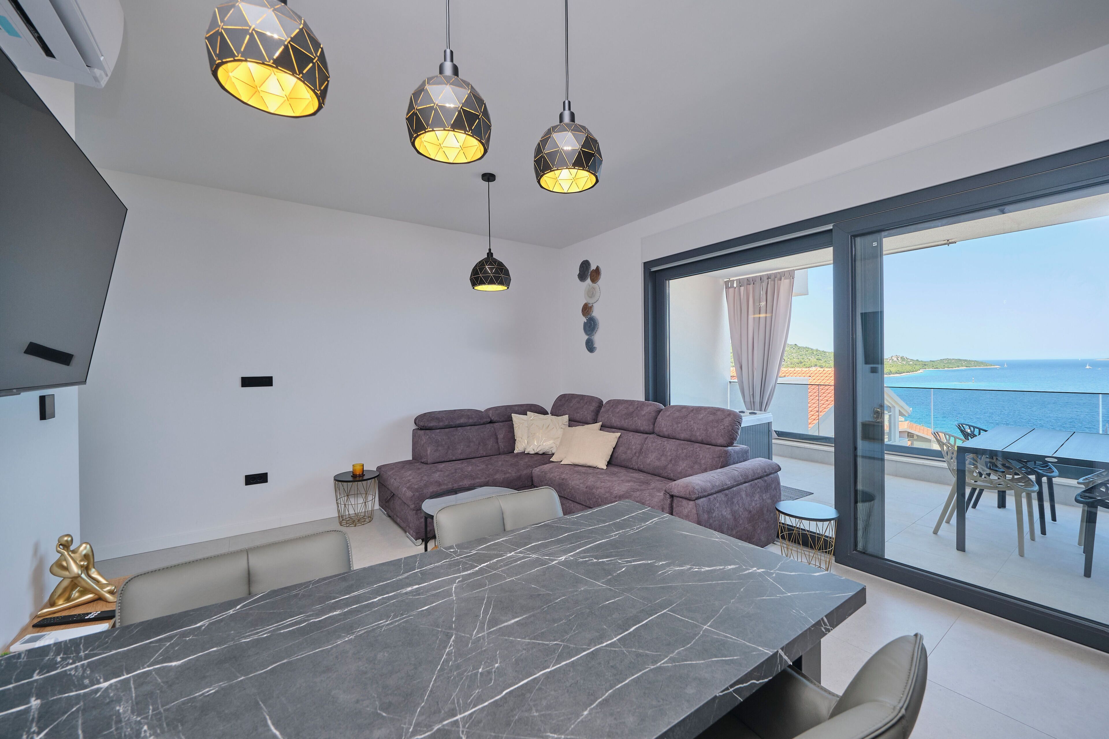 A modern living space with a dining area, a sofa, and a view of the sea.