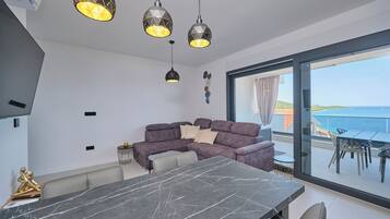 A modern living space with a dining area, a sofa, and a view of the sea.