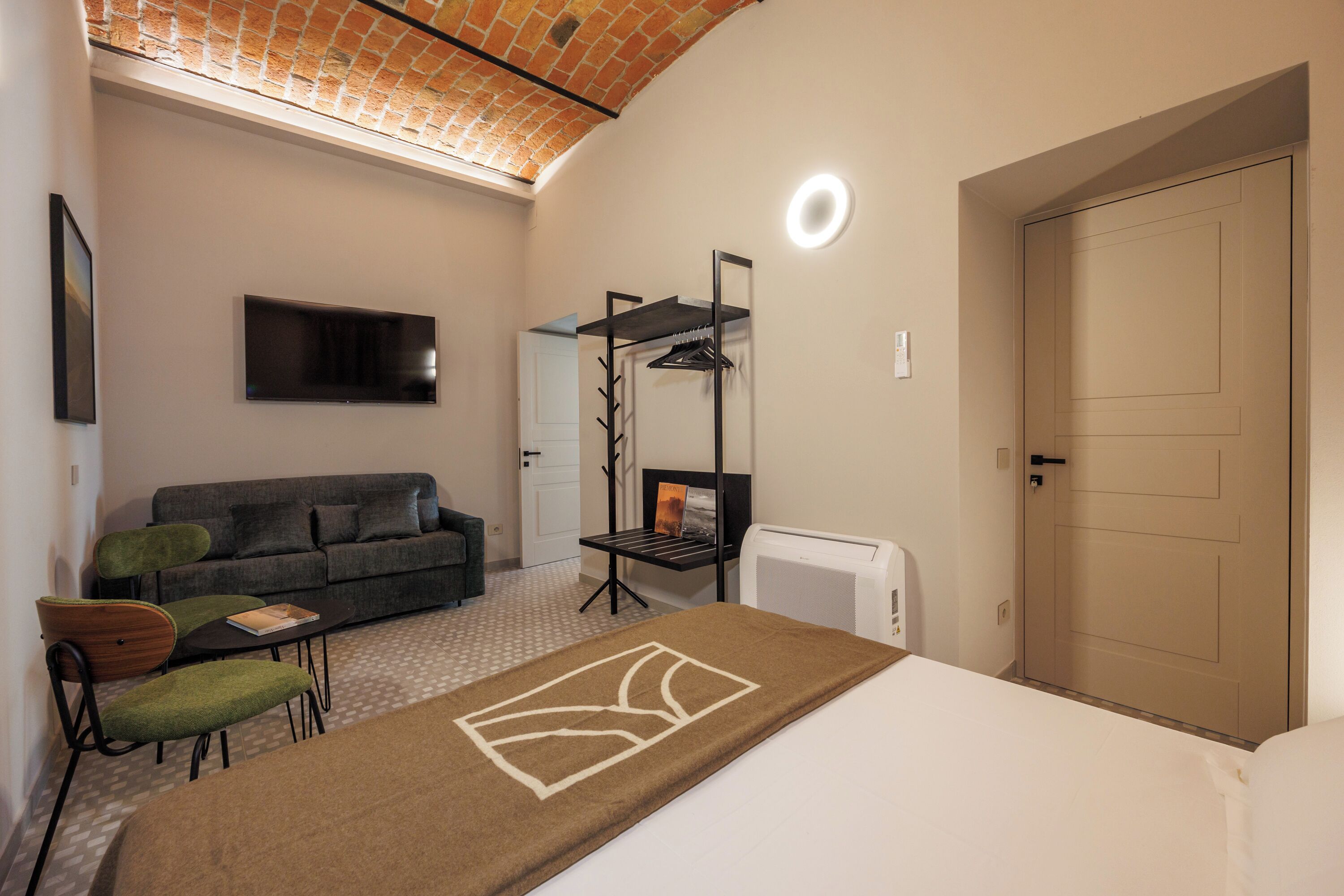 A hotel room with a bed, a sofa, a TV, a desk, and a radiator.