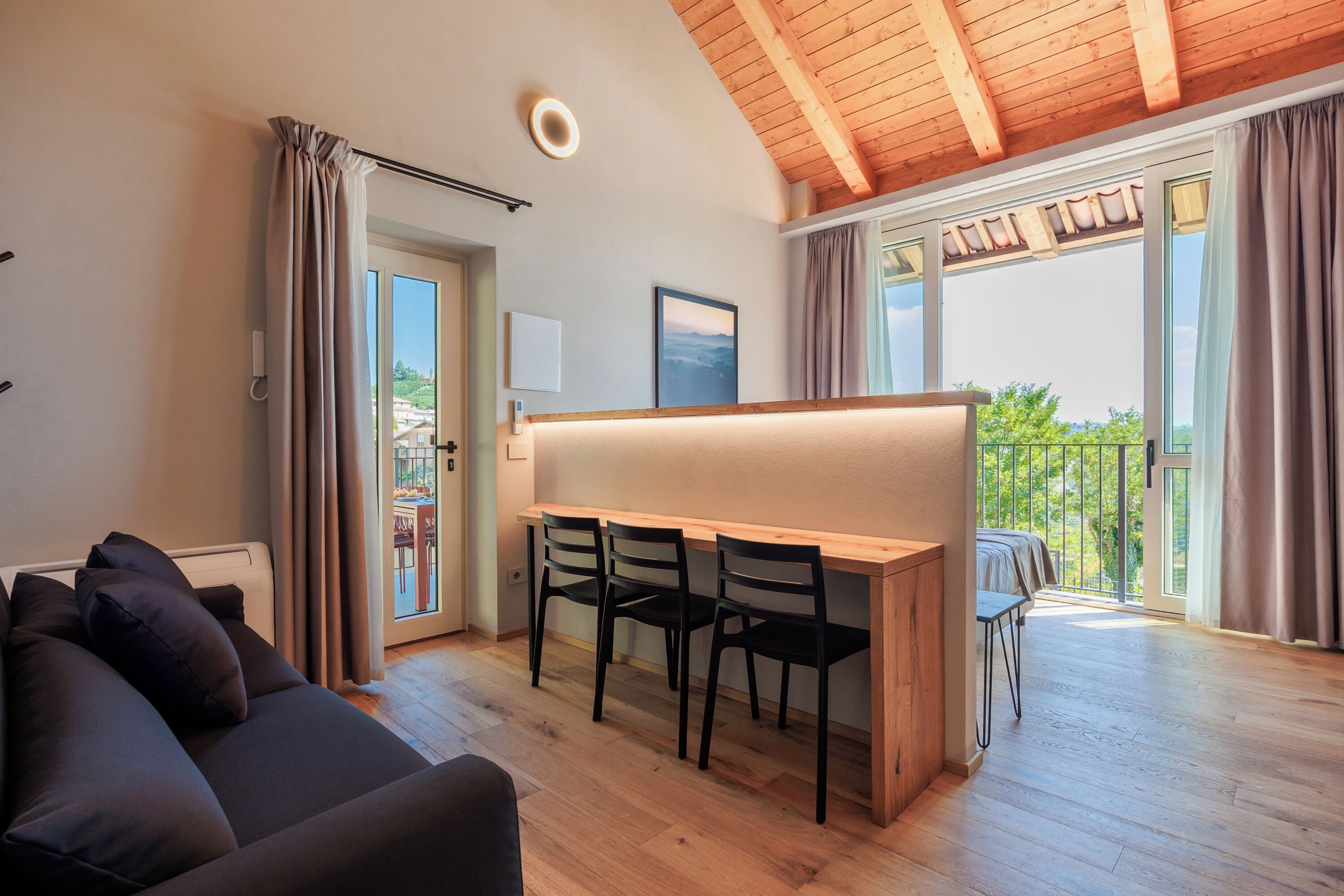 Una sala de estar moderna con techo de madera, un sofá, una mesa de comedor con sillas y un balcón con vistas.