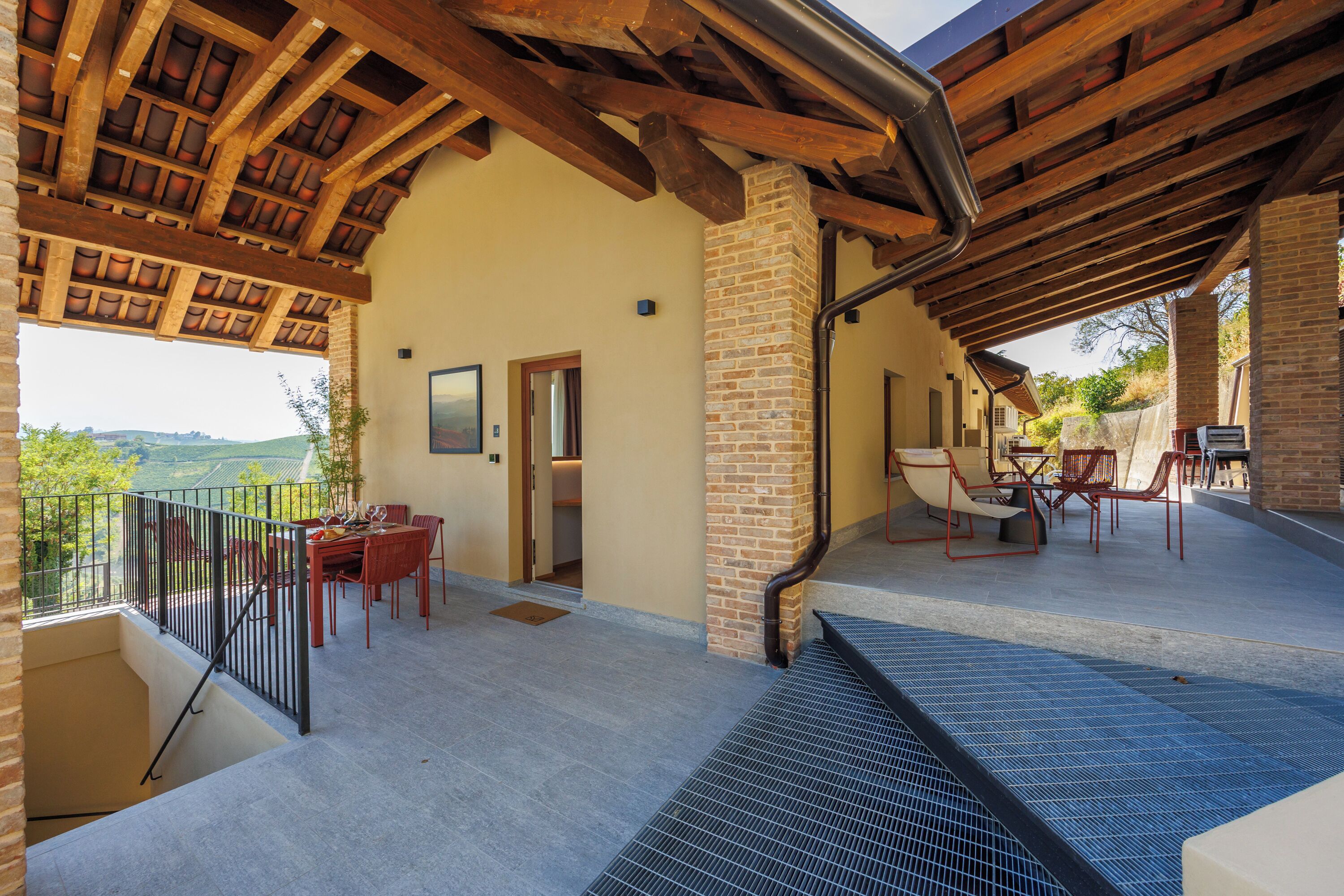 A covered outdoor area with a dining table and chairs, a view of the landscape, and a brick wall.