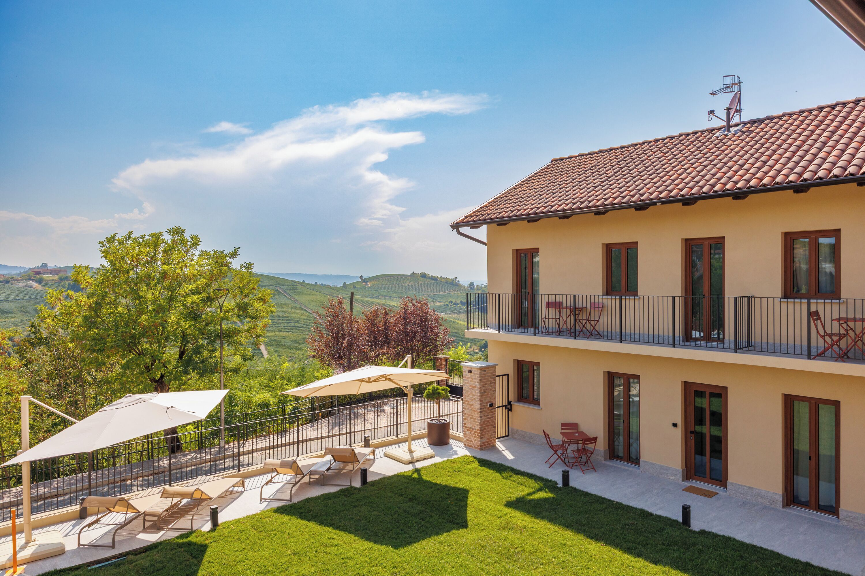 A two-story house with a balcony, outdoor seating, and a view of the countryside.