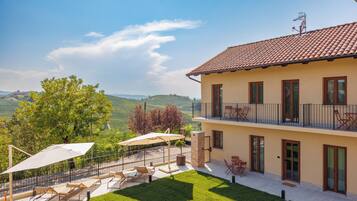 A two-story house with a balcony, outdoor seating, and a view of the countryside.