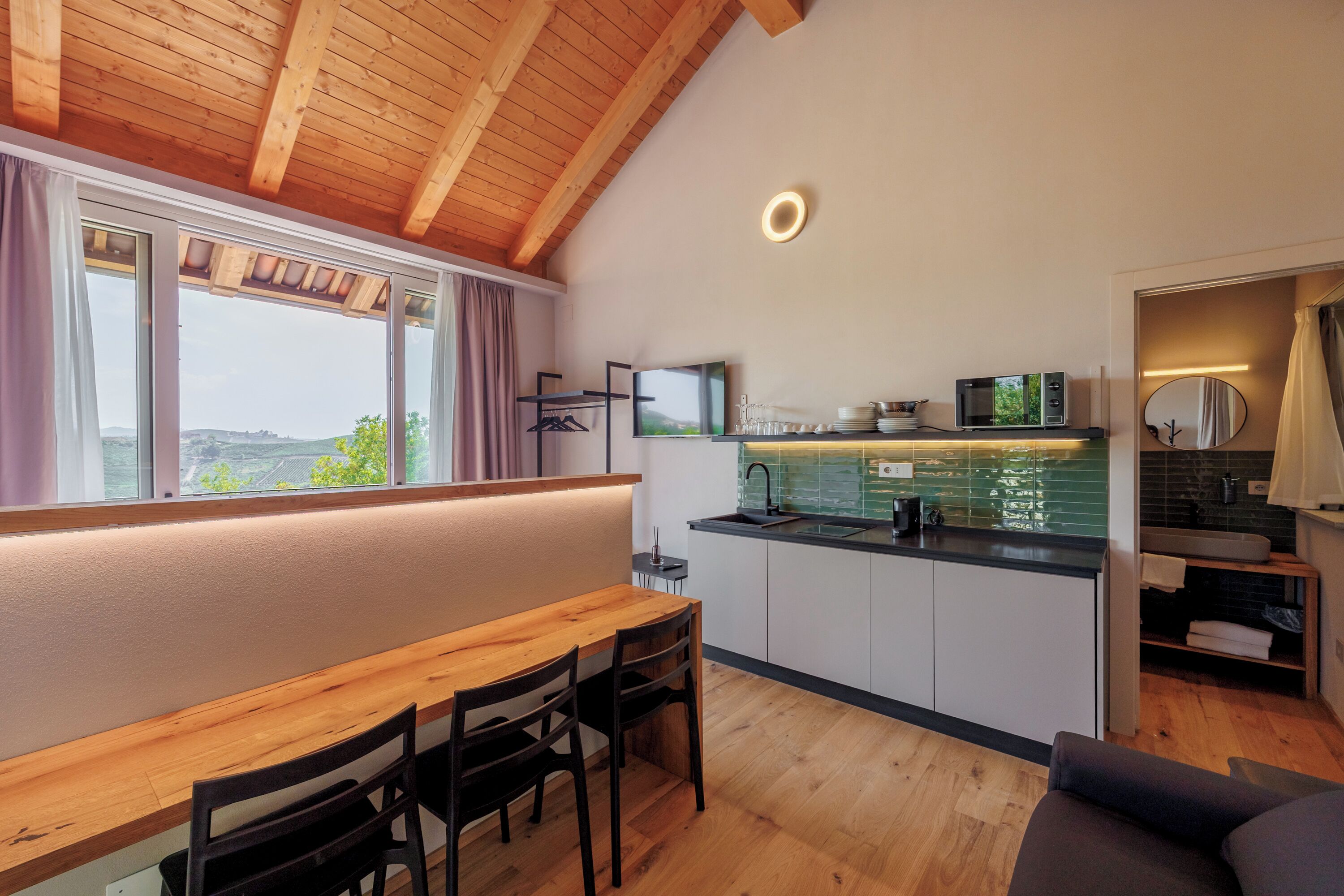 A modern kitchen with a wooden ceiling, a dining area with a table and chairs, and a view through a window.