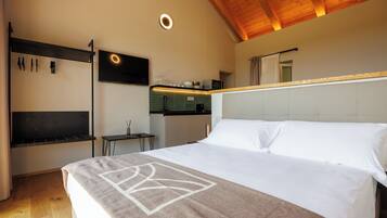 Ein Hotelzimmer mit Bett, Wandfernseher, kleinem Tisch und einer Küchenzeile.