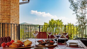 A table set with wine glasses, plates, and bread on a balcony with a view of greenery and hills. - Calanga (Barbaresco)