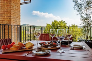 A table set with wine glasses, plates, and bread on a balcony with a view of greenery and hills. - Calanga (Barbaresco)