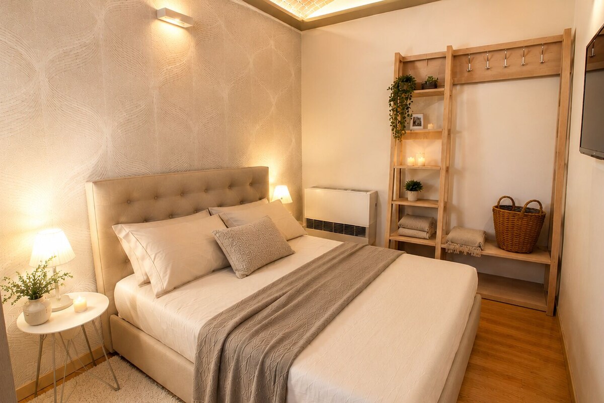 A bedroom with a bed, bedside lamps, a radiator, a wooden shelf with a plant, and a TV mounted on the wall.
