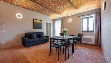 Una sala de estar moderna con techo de ladrillo, un sofá negro, una mesa de comedor con sillas y un ventanal con cortinas.