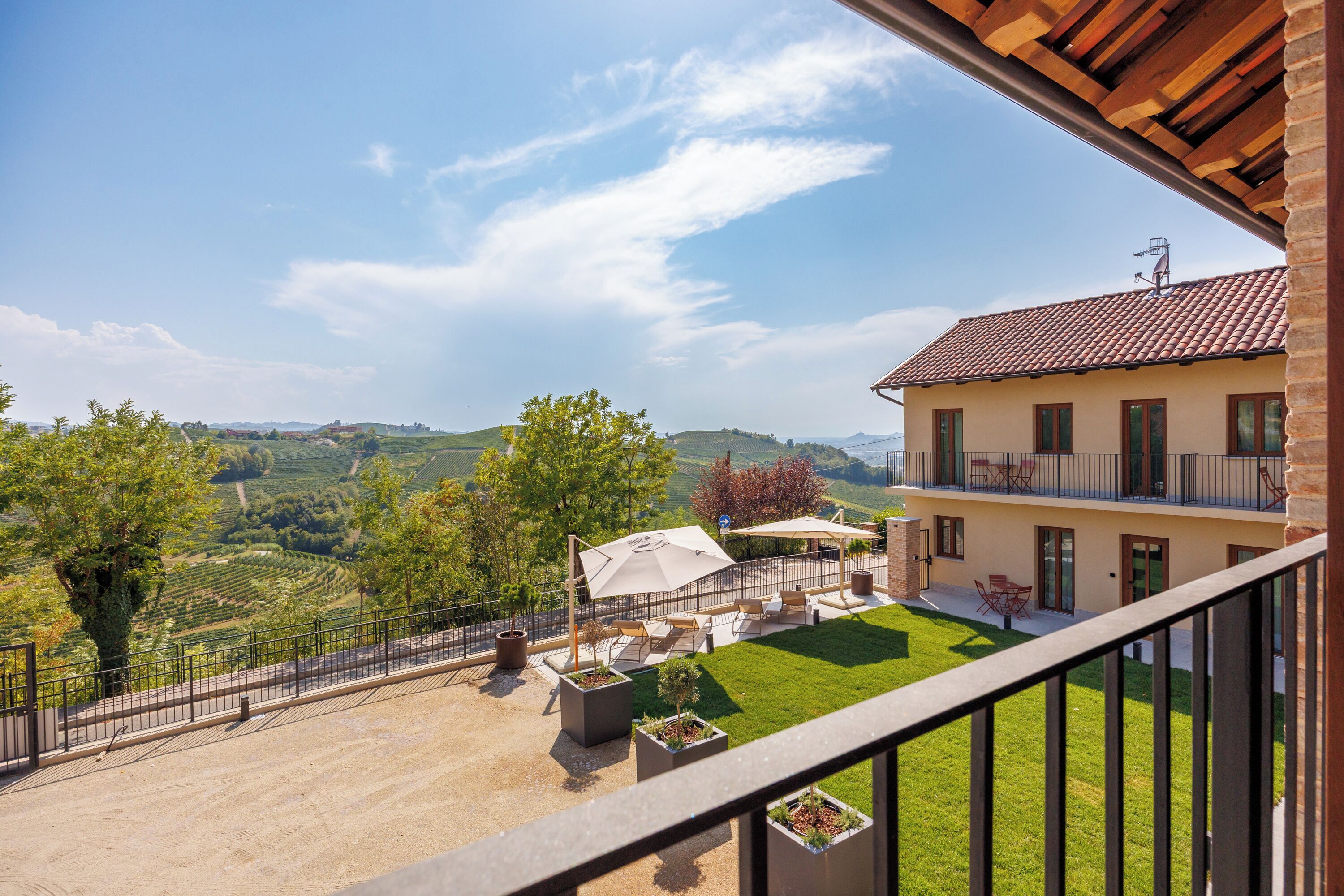 A balcony with a view of a vineyard, a terrace with outdoor furniture, and a building with a tiled roof.