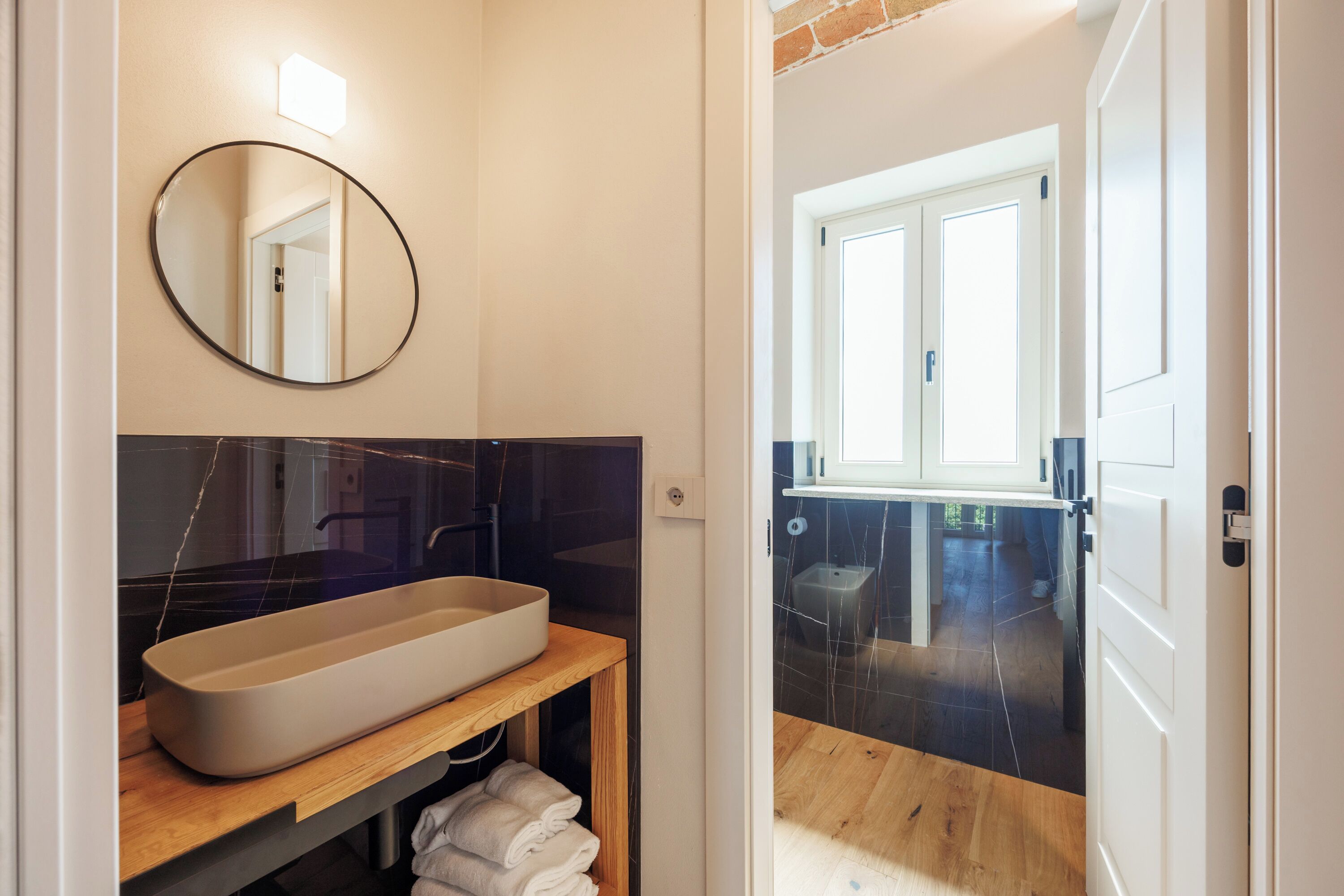 Une salle de bain moderne avec un grand lavabo ovale, un miroir rond et un meuble-lavabo en bois.