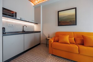 A compact living space with a kitchenette, a sofa, and a painting on the wall. - Calanga (Barbaresco)