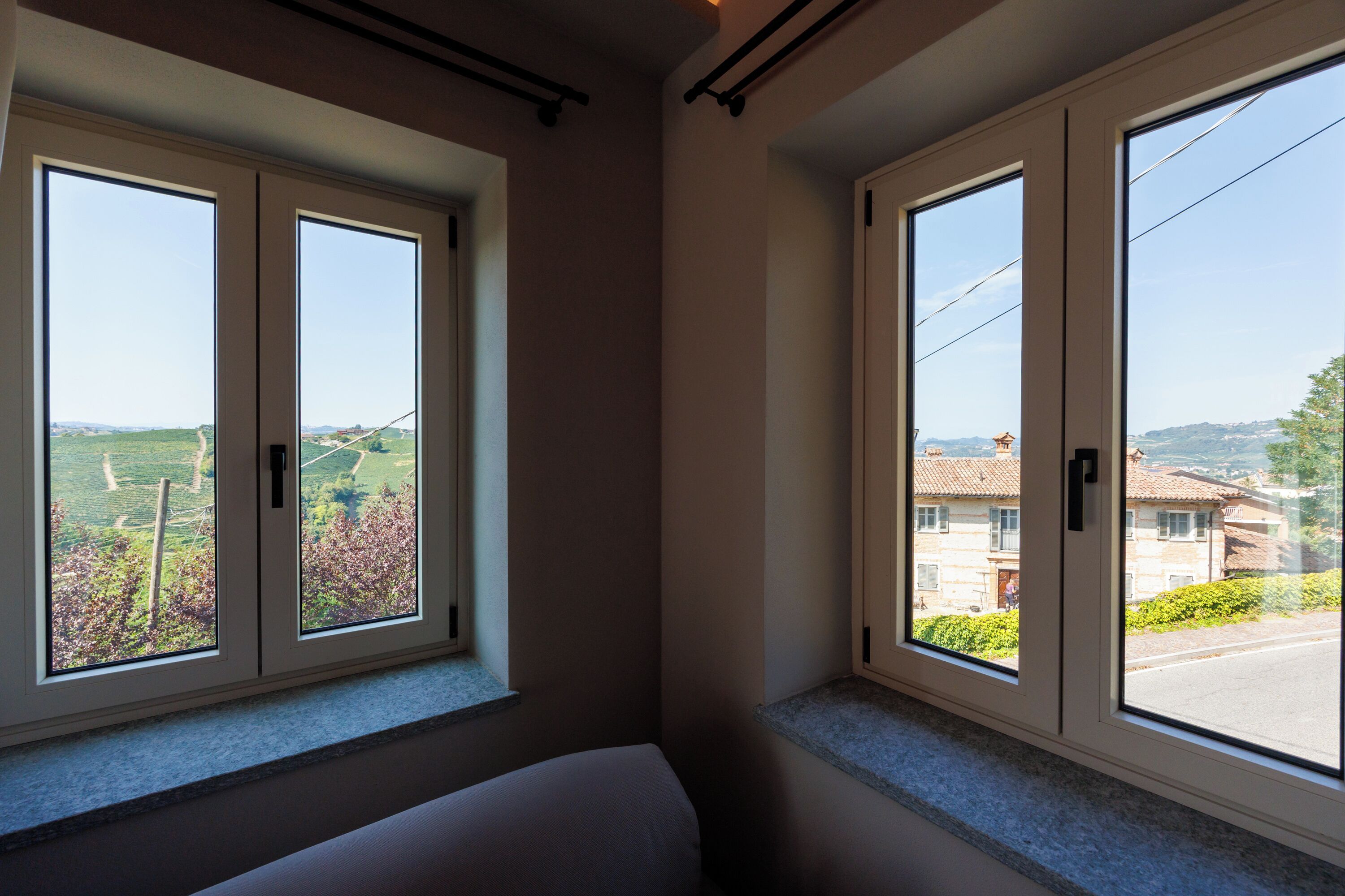 Una stanza con due ampie finestre, un letto e vista su un paesaggio rurale.