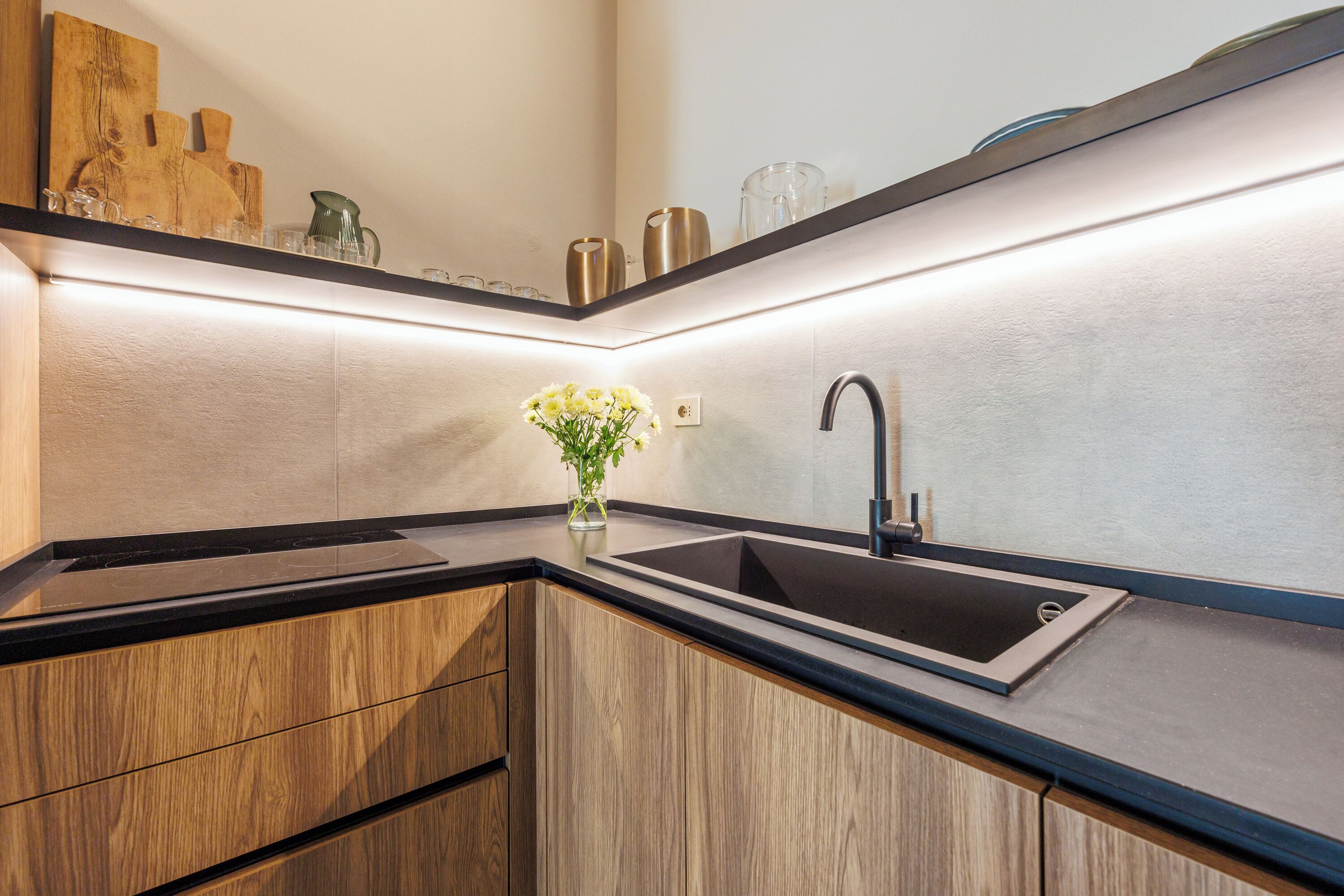 Eine moderne Küche mit schwarzem Arbeitsplatz, Holzschränken, einer Edelstahlspüle und einer Vase mit Blumen.