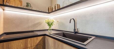 A modern kitchen with a black countertop, wooden cabinets, a stainless steel sink, and a vase with flowers.