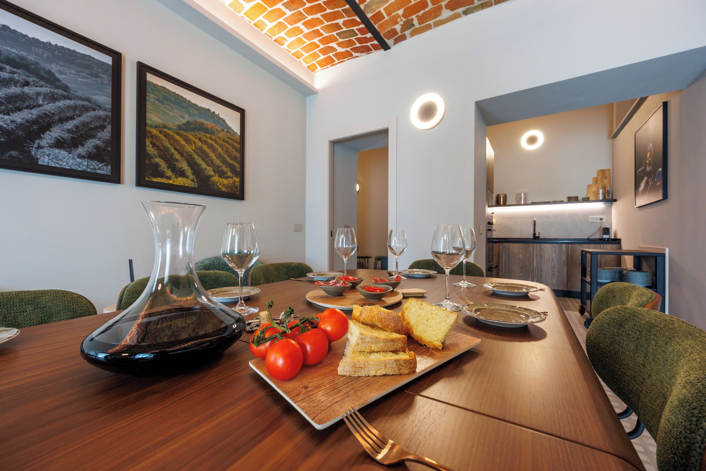 A dining area with a wooden table set for a meal, including bread, tomatoes, and wine glasses.
