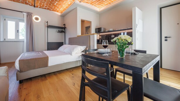 A modern hotel room with a bed, a dining table, and a kitchen area. - Calanga (Barbaresco)