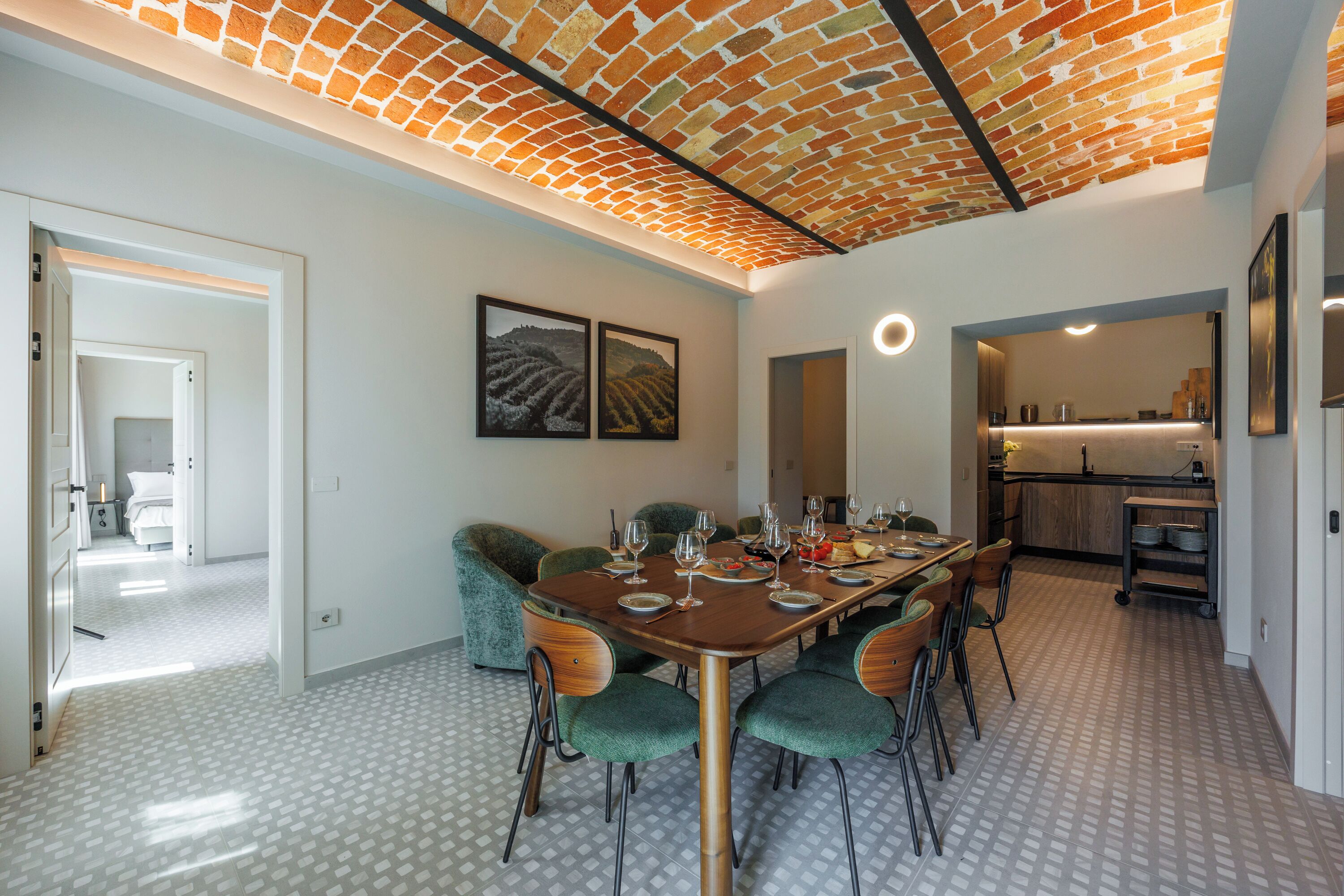 A dining area with a brick ceiling, a large table set for six, and green upholstered chairs.