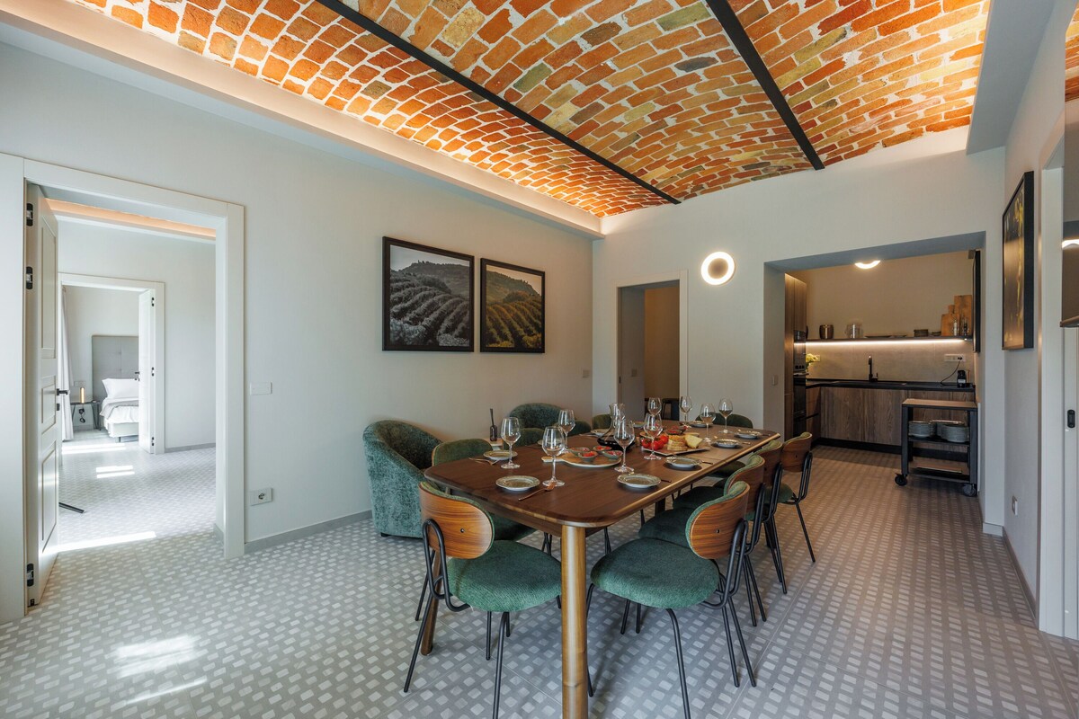 A dining area with a brick ceiling, a large table set for six, and green upholstered chairs.