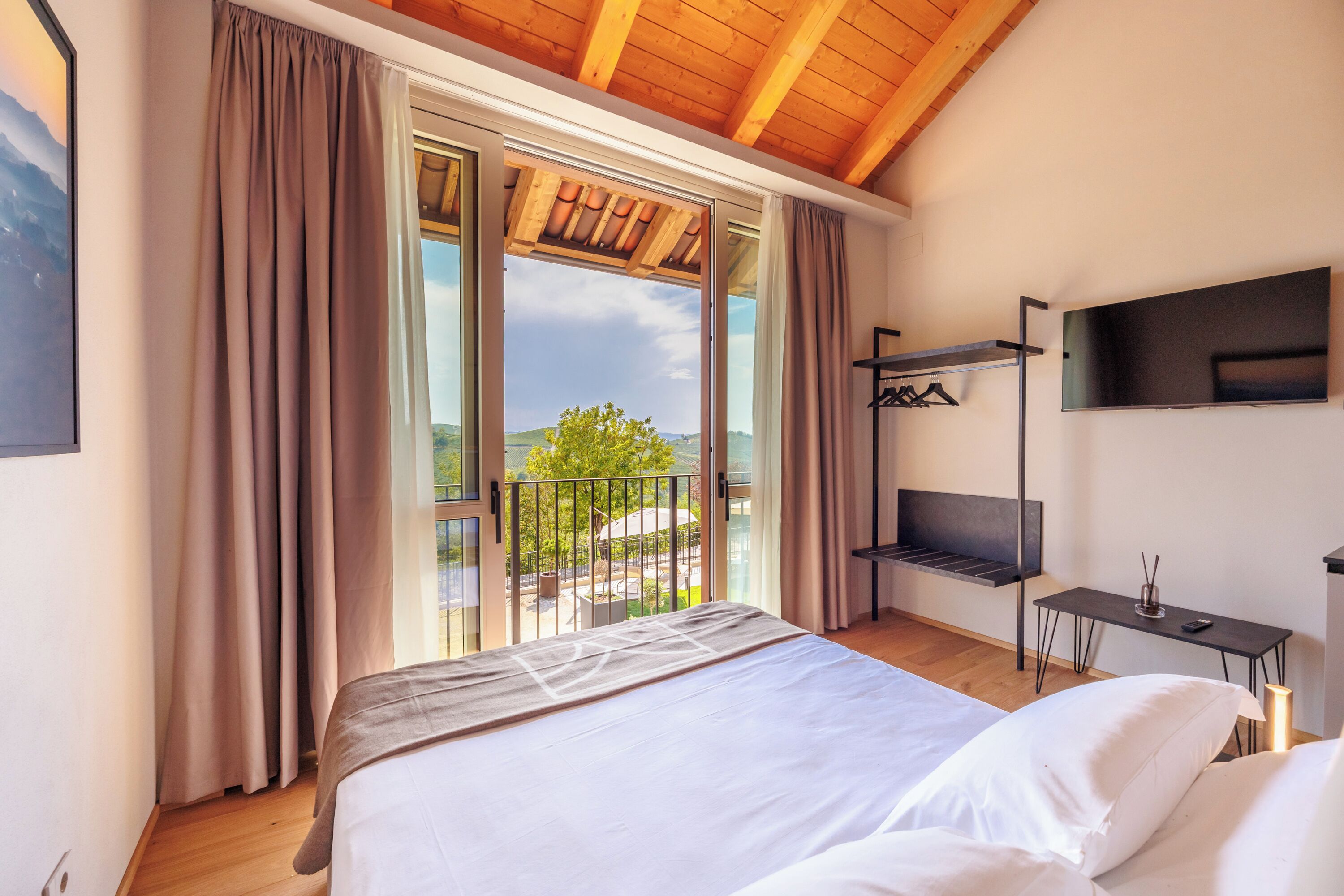 Een slaapkamer met een groot bed, een aan de muur bevestigde televisie en een balkon met uitzicht op de omgeving.