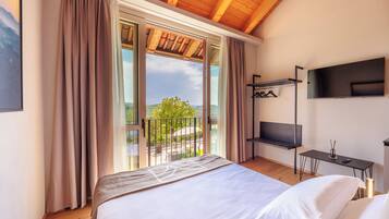 Een slaapkamer met een groot bed, een aan de muur bevestigde televisie en een balkon met uitzicht op de omgeving.